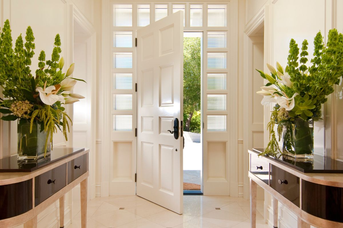 A hallway featuring a white door and elegant vases filled with colorful flowers, creating a welcoming atmosphere.